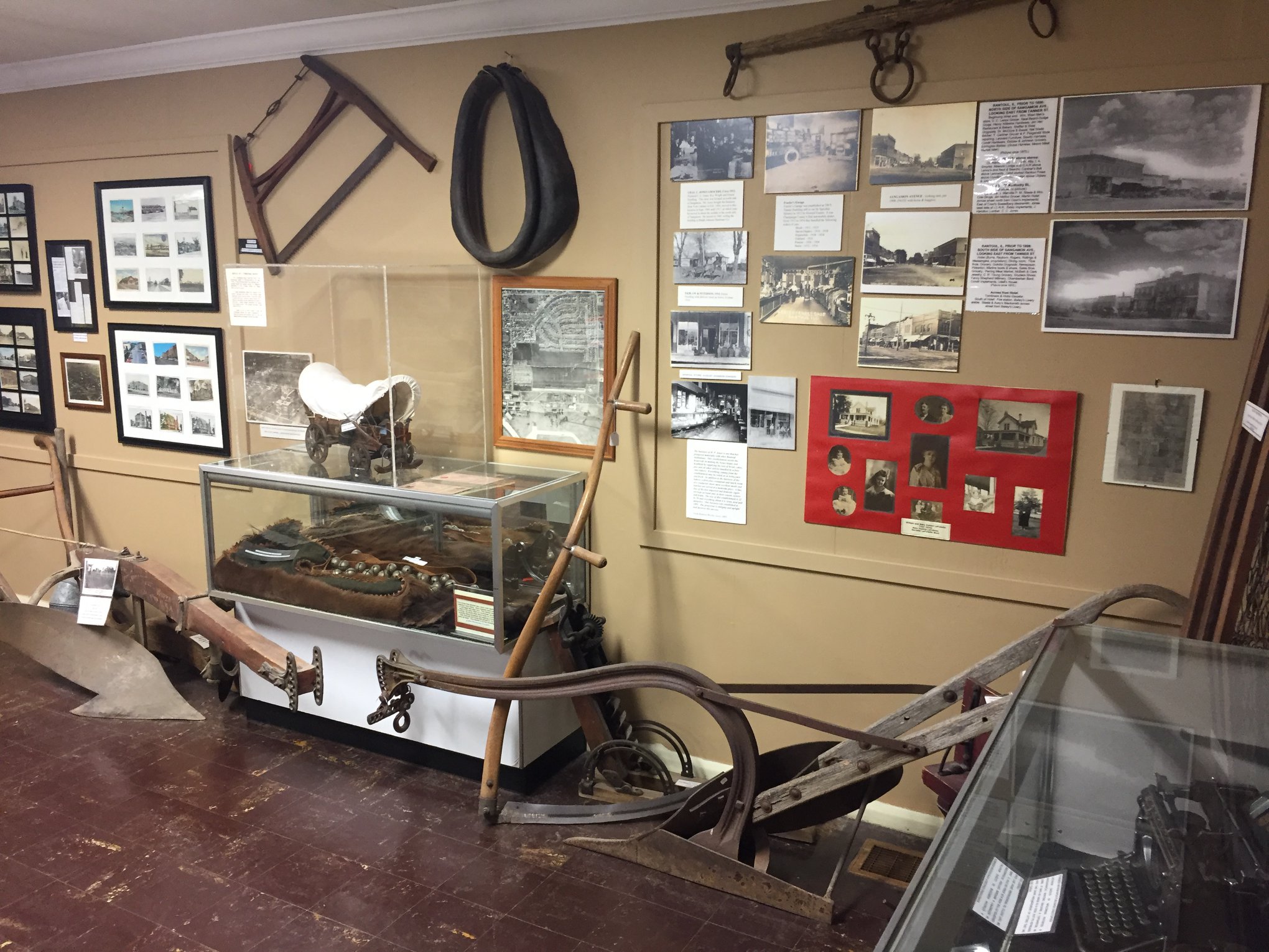 A museum wall of historical photos with vintage horse-drawn plows in the foreground.